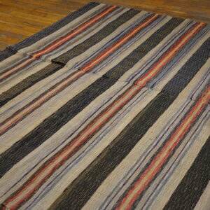 Flatwoven striped rug stitched together, featuring black, beige, red, and blue colors on wood flooring.