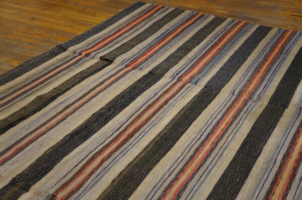 Flatwoven striped rug stitched together, featuring black, beige, red, and blue colors on wood flooring.