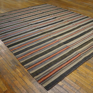 Striped flatweave rug in black, beige, red, and blue colors lying on rustic wood flooring.