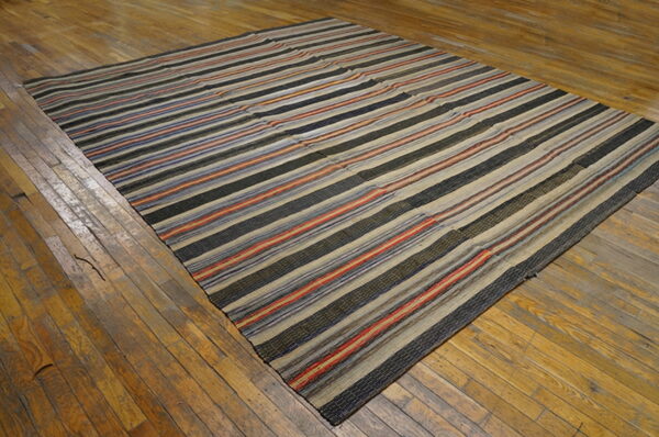 Striped flatweave rug in black, beige, red, and blue colors lying on rustic wood flooring.