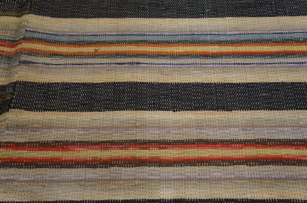 A chunky woven rug features horizontal stripes in navy, beige, purple, red, orange, and assorted muted colors.