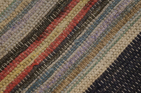 Diagonal multicolored striped rug featuring a thick, chunky woven texture in red, blue, tan, and black.