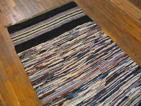 Multicolor striped flatweave rug with a solid black stripe section resting on warm wooden flooring.