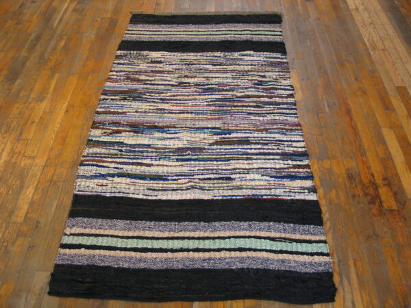 Flatweave rag rug runner with multicolored horizontal stripes and contrasting solid black ends on wood planks.