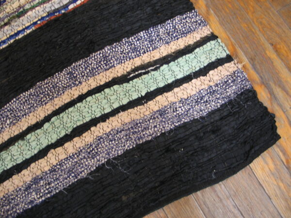 Chunky flatweave rag rug featuring stripes of black, mint, beige, and speckled blue on wood flooring.