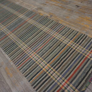 A low-pile runner with a multicolored plaid pattern rests on distressed gray wooden floors.
