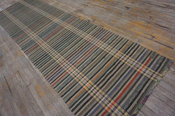 A low-pile runner with a multicolored plaid pattern rests on distressed gray wooden floors.