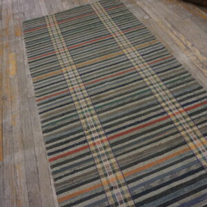 A flatwoven runner rug with horizontal stripes and vertical plaid bands lies on distressed gray wood flooring.