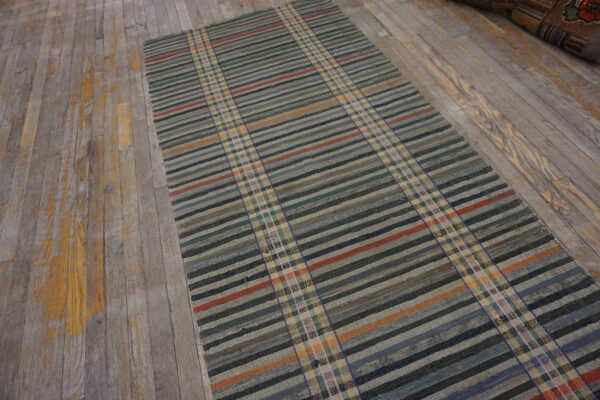 A flatwoven runner rug with horizontal stripes and vertical plaid bands lies on distressed gray wood flooring.