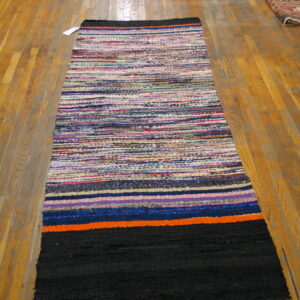 Woven runner rug featuring multicolored stripes and large sections of black, orange, and blue on wood planks.