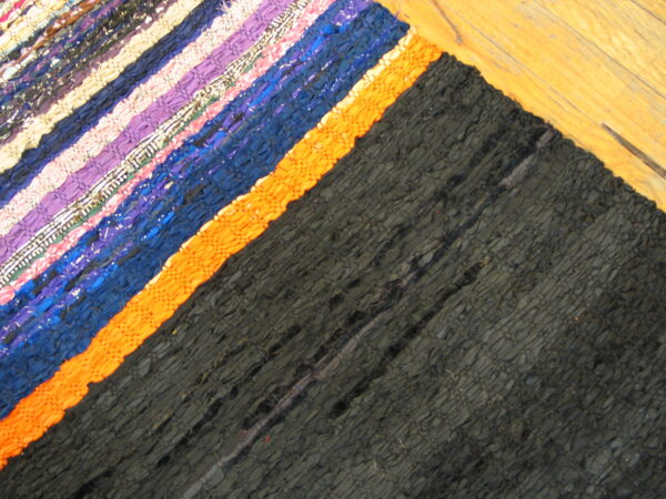 A multi-colored woven rug with black, orange, purple, and blue diagonal stripes rests on wood flooring.