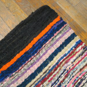 Close-up of a woven striped rug with colorful rag texture and a solid black corner on wood.