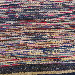 Close-up of a multicolored, textured, flat-woven rag rug with horizontal stripes on wood flooring.