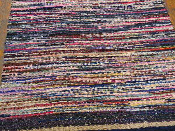 Close-up of a multicolored, textured, flat-woven rag rug with horizontal stripes on wood flooring.