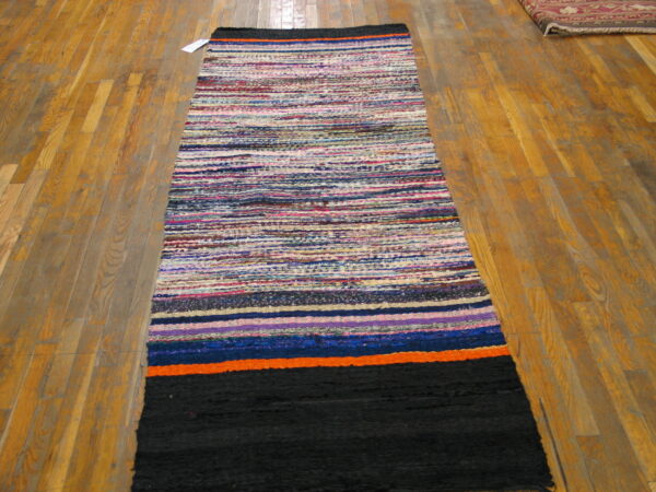 Multicolored striped runner rug with a solid black end panel on light hardwood flooring.