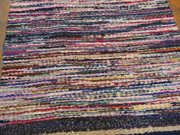 Flat-woven, multicolored rag rug with chunky horizontal stripes lies on wood planks.