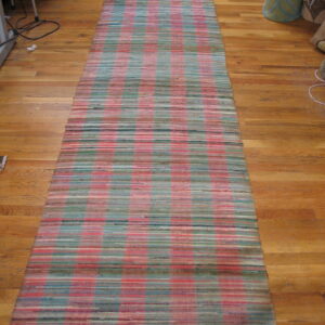 A woven rag rug runner featuring a plaid pattern of pink, teal, and green lies on a wood floor.