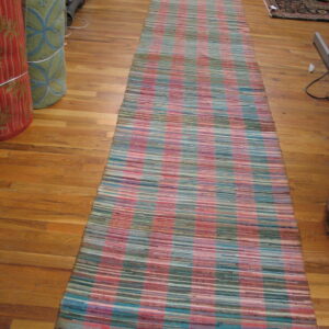 A long, flat-weave runner rug with pink, teal, and khaki stripes rests on a light wood floor.