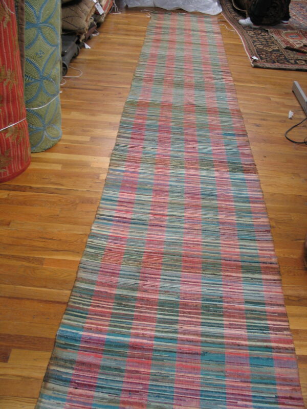 A long, flat-weave runner rug with pink, teal, and khaki stripes rests on a light wood floor.