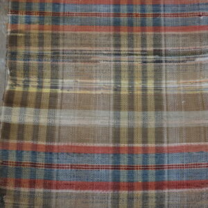 Flatwoven plaid rug in earth tones, blue, and red stripes lying on weathered gray wood floorboards.