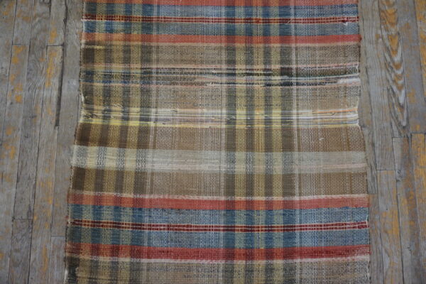 Flatwoven plaid rug in earth tones, blue, and red stripes lying on weathered gray wood floorboards.