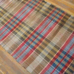 Low-profile plaid runner rug with brown, tan, blue, and red stripes lying on wood planks.