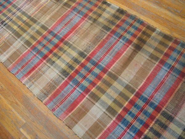 Low-profile plaid runner rug with brown, tan, blue, and red stripes lying on wood planks.
