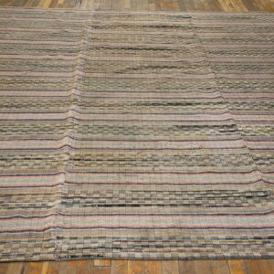 Flatweave rug with neutral stripes, checkerboard patterns, and pink accents lies on rustic hardwood flooring.