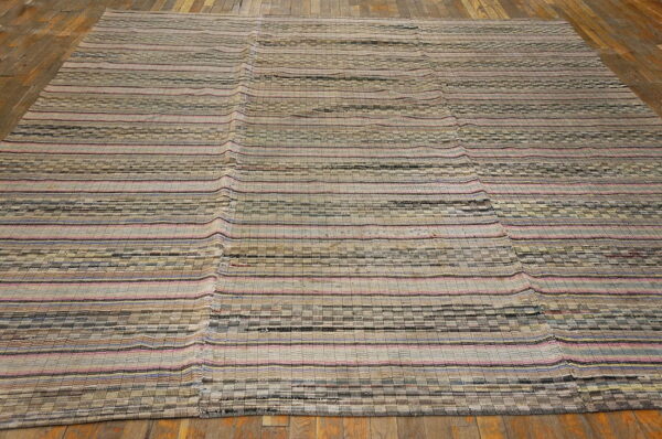 Flatweave rug with neutral stripes, checkerboard patterns, and pink accents lies on rustic hardwood flooring.