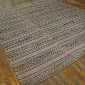 Textured flat-weave rug featuring beige, pink, and dark striped panels resting on worn wooden floorboards.
