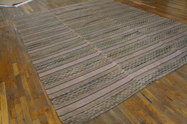 Textured flat-weave rug featuring beige, pink, and dark striped panels resting on worn wooden floorboards.
