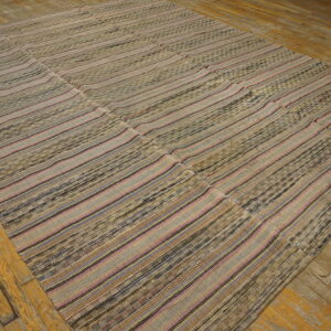 Flat woven rug featuring horizontal stripes of beige, brown, pink, and blue on distressed wood floor.