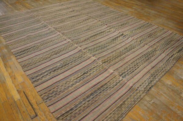 Flat woven rug featuring horizontal stripes of beige, brown, pink, and blue on distressed wood floor.