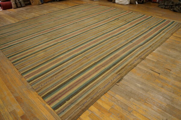 Flatwoven rug featuring wide vertical stripes in tan, muted green, and red on distressed hardwood flooring.