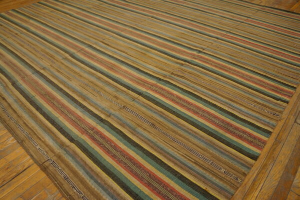 Flatweave striped rug in tan, teal, red, and dark brown, showing panel seams on hardwood floor.