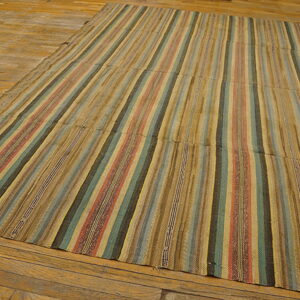 Low-profile rug with vertical stripes of muted tan, red, teal, and brown on wood flooring.
