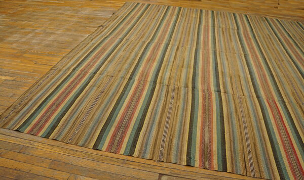 Low-profile rug with vertical stripes of muted tan, red, teal, and brown on wood flooring.