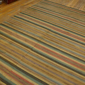 Flat-woven rug with multicolored stripes in tan, teal, and rust on distressed wood flooring.