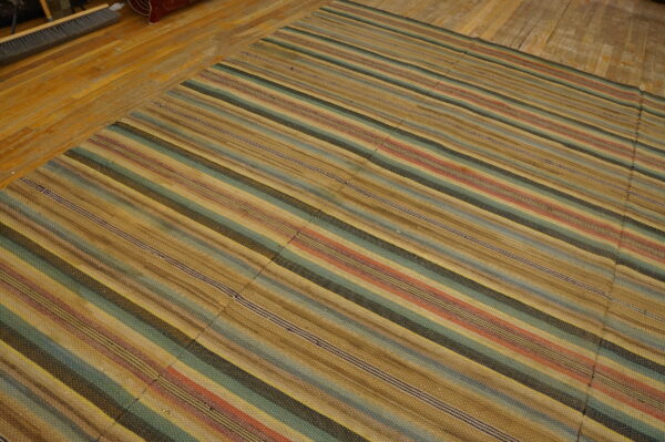 Flat-woven rug with multicolored stripes in tan, teal, and rust on distressed wood flooring.