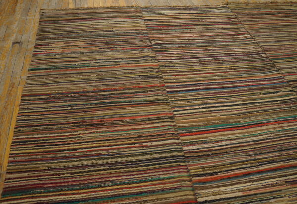 Low pile rug with variegated horizontal stripes in mixed earth tones rests on peeling yellow wood planks.
