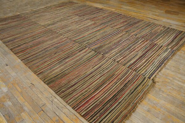 Large, flatwoven rug with multicolor vertical stripes lies on rustic, light-colored wood flooring.