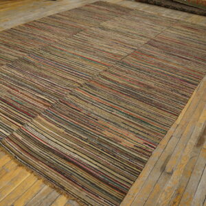 A large, pieced flatweave rug with multicolored horizontal stripes rests on worn wood flooring.