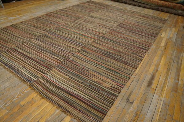 A large, pieced flatweave rug with multicolored horizontal stripes rests on worn wood flooring.