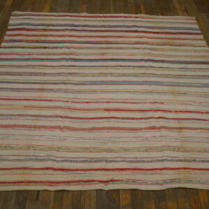 Cream rug featuring horizontal stripes of red, blue, and yellow threads on rustic wood flooring.