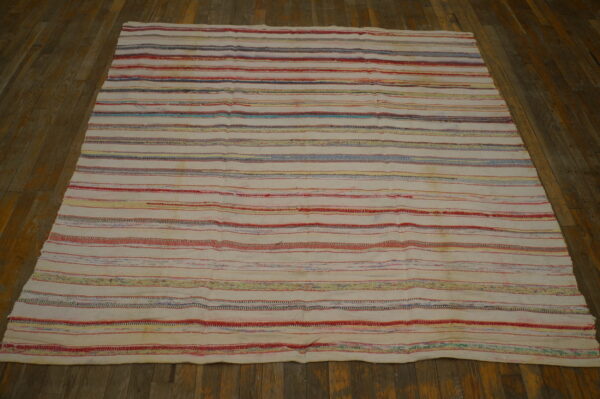 Cream rug featuring horizontal stripes of red, blue, and yellow threads on rustic wood flooring.
