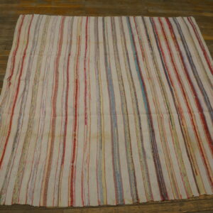 White rug with thin, multicolored vertical stripes, including red and blue, displayed on a rustic wood floor.