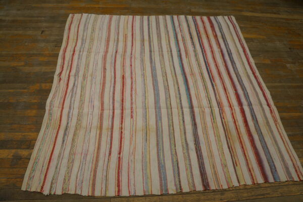 White rug with thin, multicolored vertical stripes, including red and blue, displayed on a rustic wood floor.