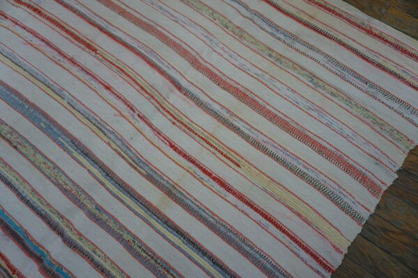Low-pile white rug featuring narrow red, yellow, blue, and variegated multicolor stripes on wood planks.