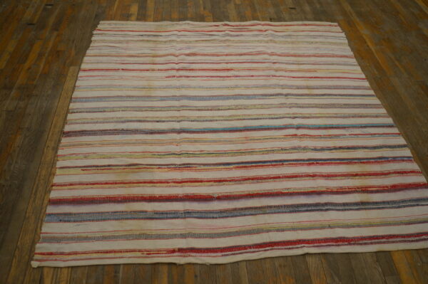 White flatweave rug with thin multicolored stripes rests on aged brown plank flooring.