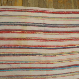 White flatweave rag rug with horizontal stripes of red, blue, gray, and yellow on wood planks.